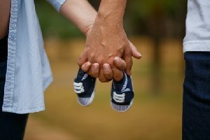 2 people holding hands with baby shoes in the middle